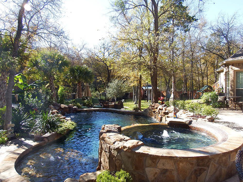 Freeform pool with raised stone spa and spillway under mature trees