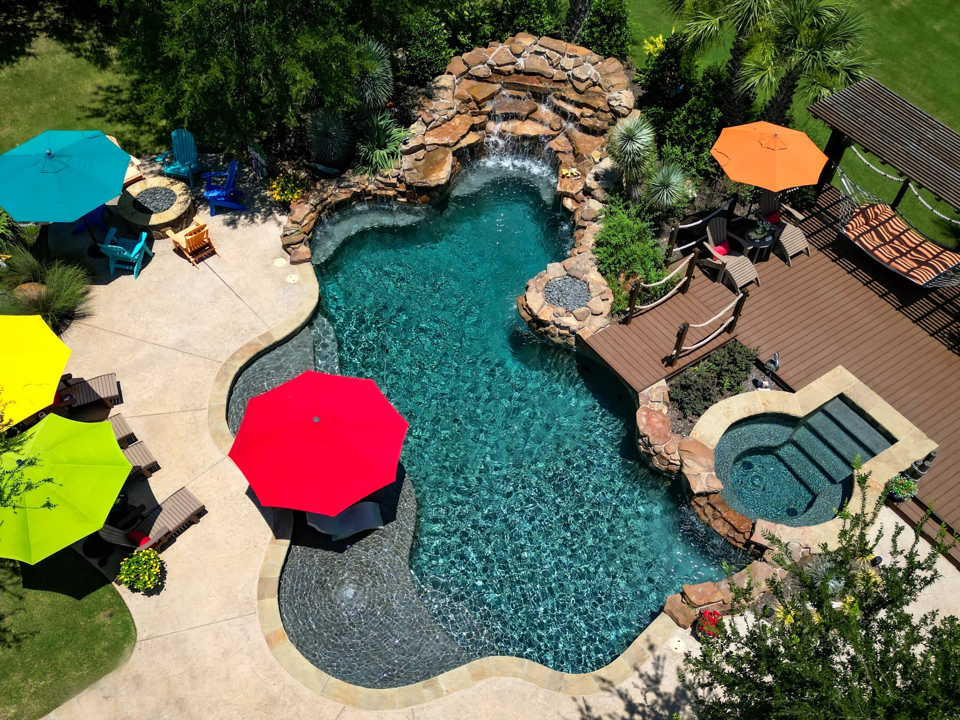 Aerial view of a Bill's Pool backyard with a freeform pool, rock waterfall, spa and colorful umbrellas