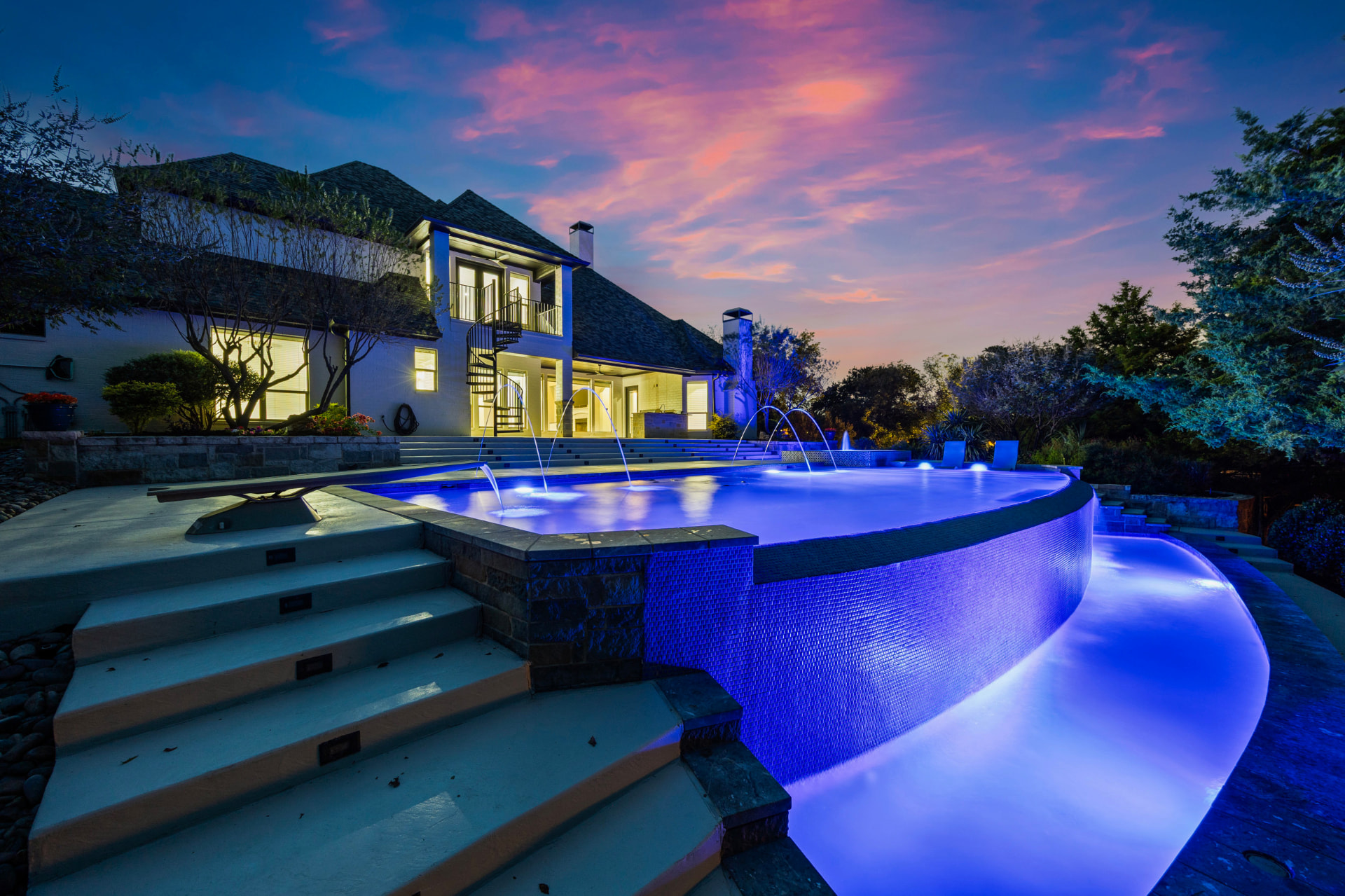 Negative edge pool with laminar water arcs and blue pool lights at dusk
